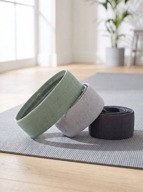 Three fabric hip bands in sage, grey and graphite on a grey yoga mat