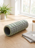 Sage green Grid Foam Roller on an oak floor next to a towel