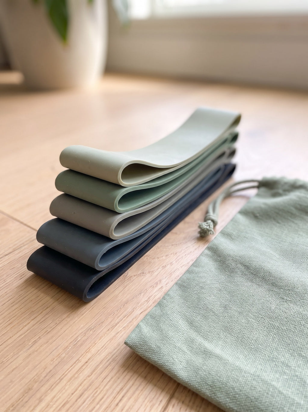 Stack of five mini loop resistance bands from pale sage to graphite