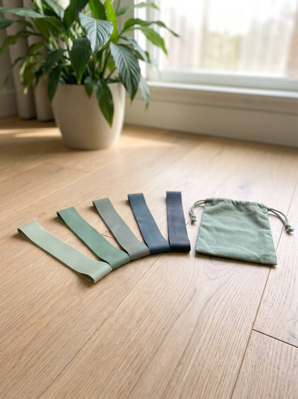 Five mini loop resistance bands fanned out on an oak floor with a sage pouch