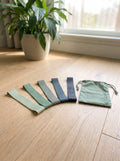 Five mini loop resistance bands fanned out on an oak floor with a sage pouch