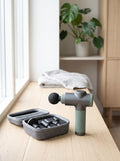 Pulse Mini Massage Gun with its zip case and spare heads on an oak floor