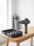 Pulse Pro Massage Gun standing next to its open hard case on a wooden bench